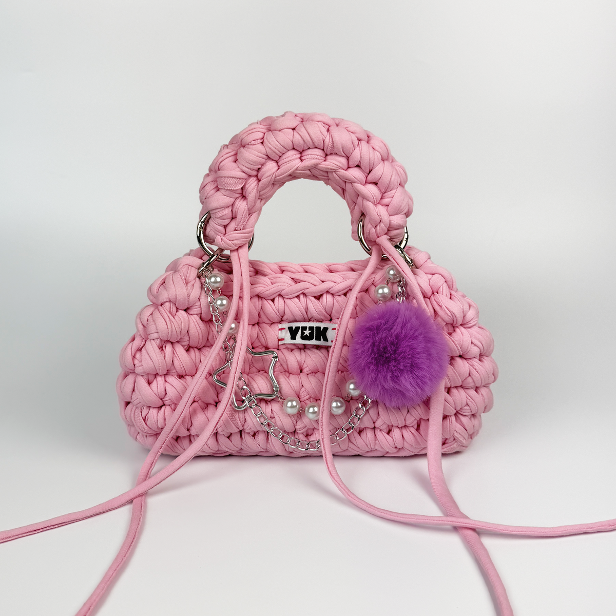Handmade crochet handbag in pink with pompom detail and a bag charm by Studio YUK